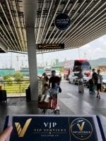 VIP meet and greet area at an airport terminal with travelers and luggage near a blue VIP counter under a covered walkway