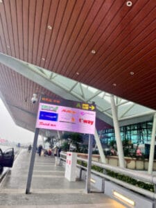 Outdoor transit walkway under a wooden ceiling with a large digital information screen showing directions and schedules